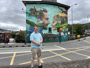 Joel James MS standing by Tee2Sugars Pontypridd mural